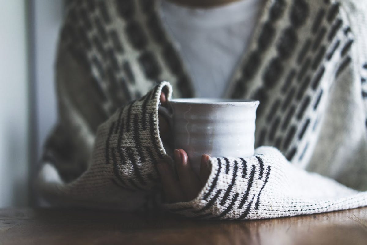 Woman wearing cardigan holding ceramic mug, drinking coffee on a cold day